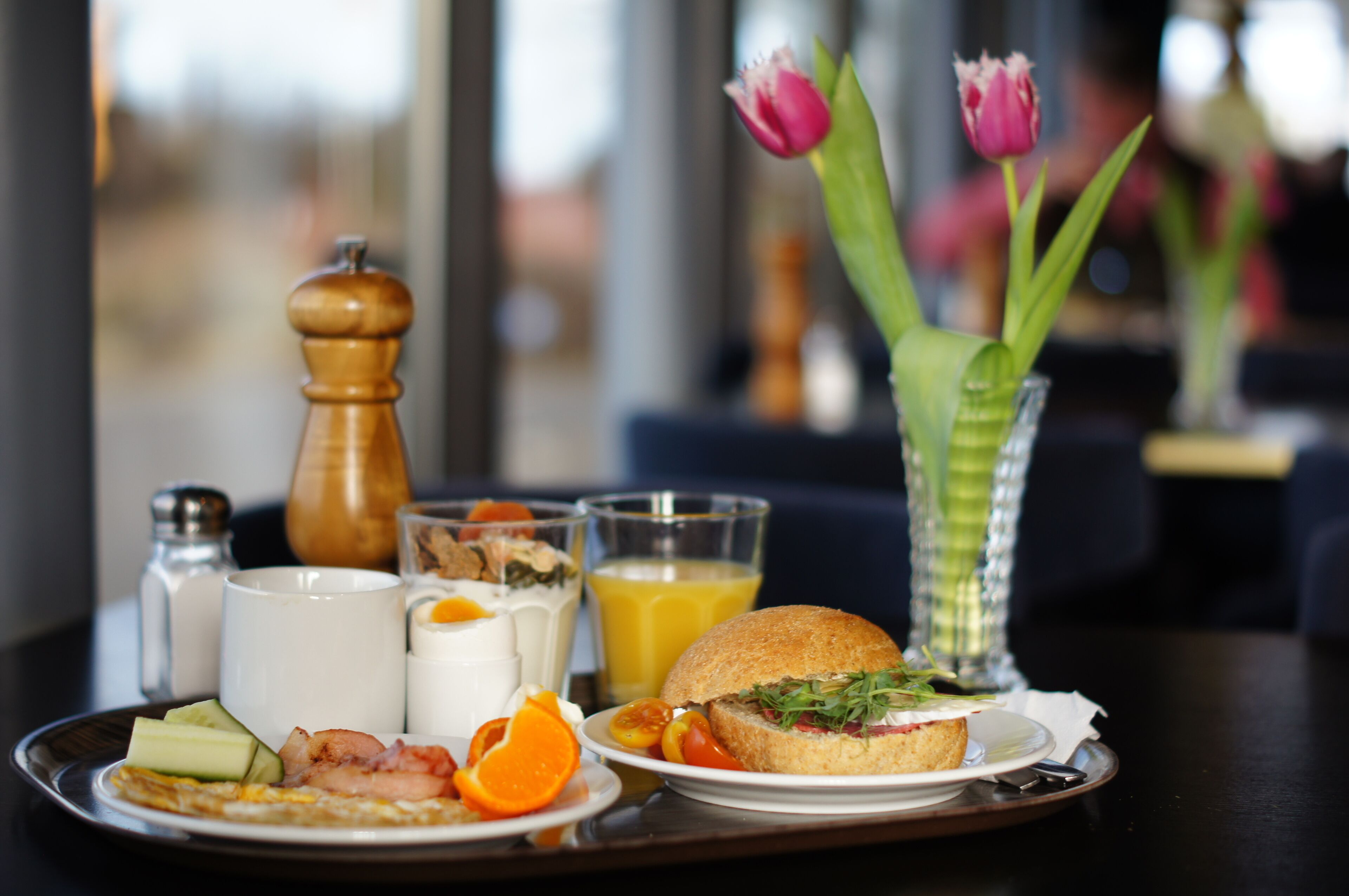 Un plateau de petit-déjeuner avec divers aliments, un verre de jus d’orange et un vase de tulipes.