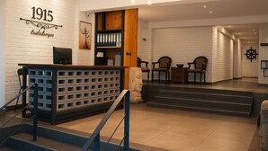 A reception area with a white brick wall, a wooden reception desk, and a staircase leading to a second floor. - Hotel 1915 Kuala Lumpur (Kuala Lumpur)