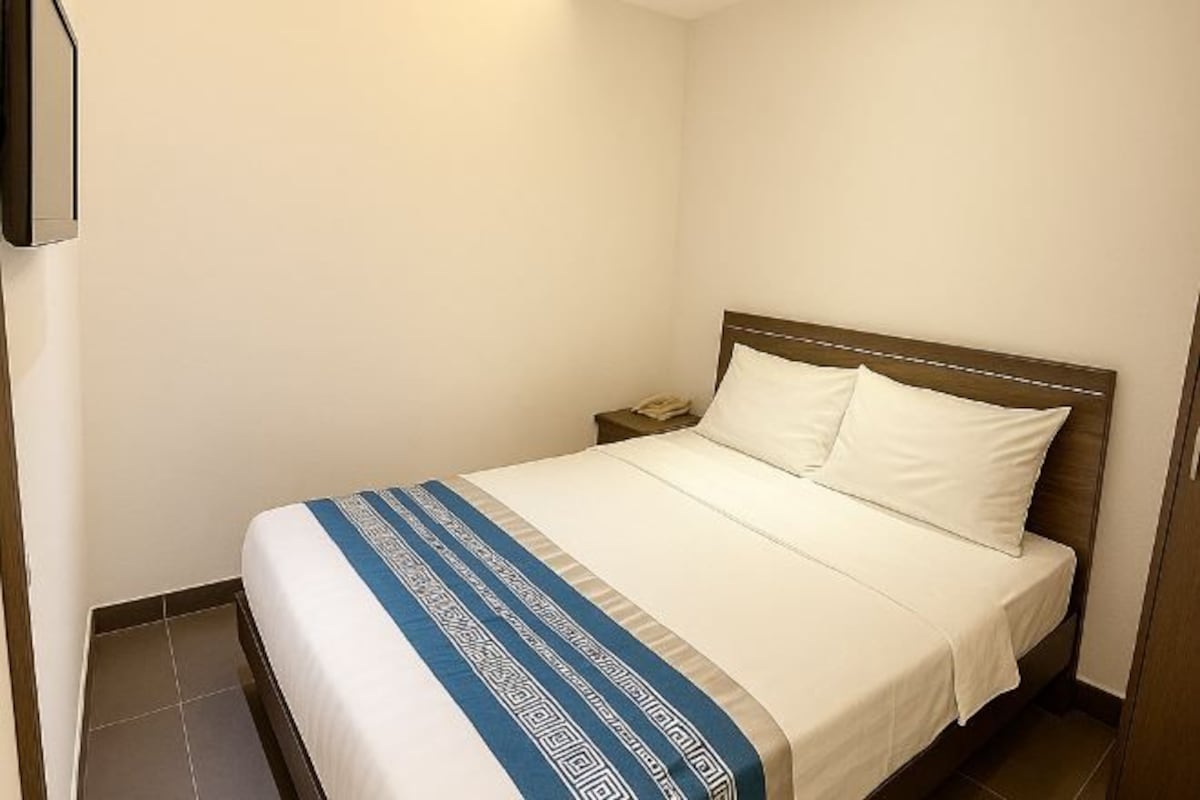 A neatly made bed with a white and blue bedspread, a wooden headboard, and a nightstand with a lamp.
