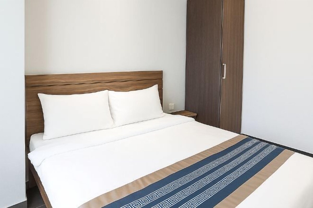 A neatly made bed with a wooden headboard, a matching nightstand, and a wardrobe with a handle.