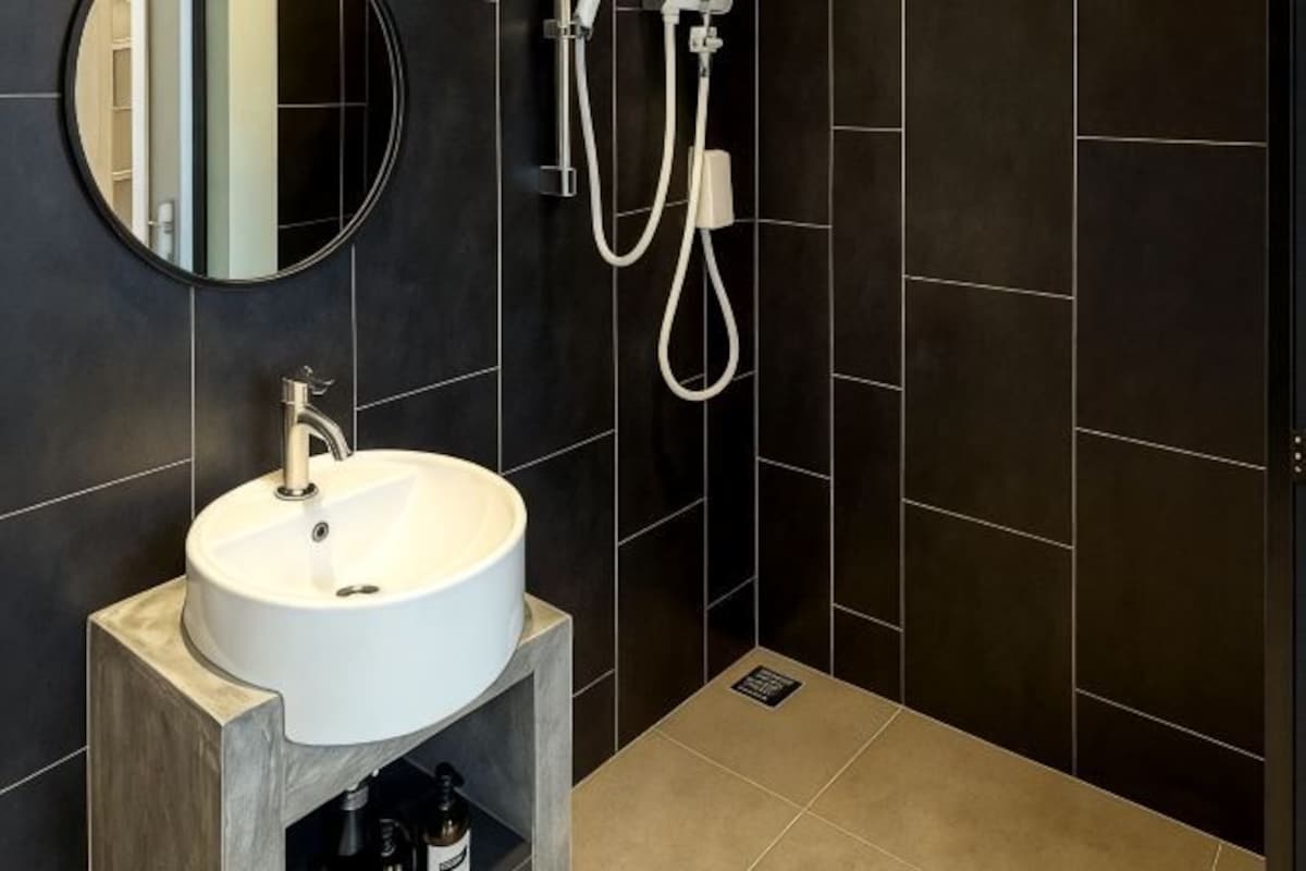A bathroom with a white sink, dark tiled walls, a mirror, and a shower.