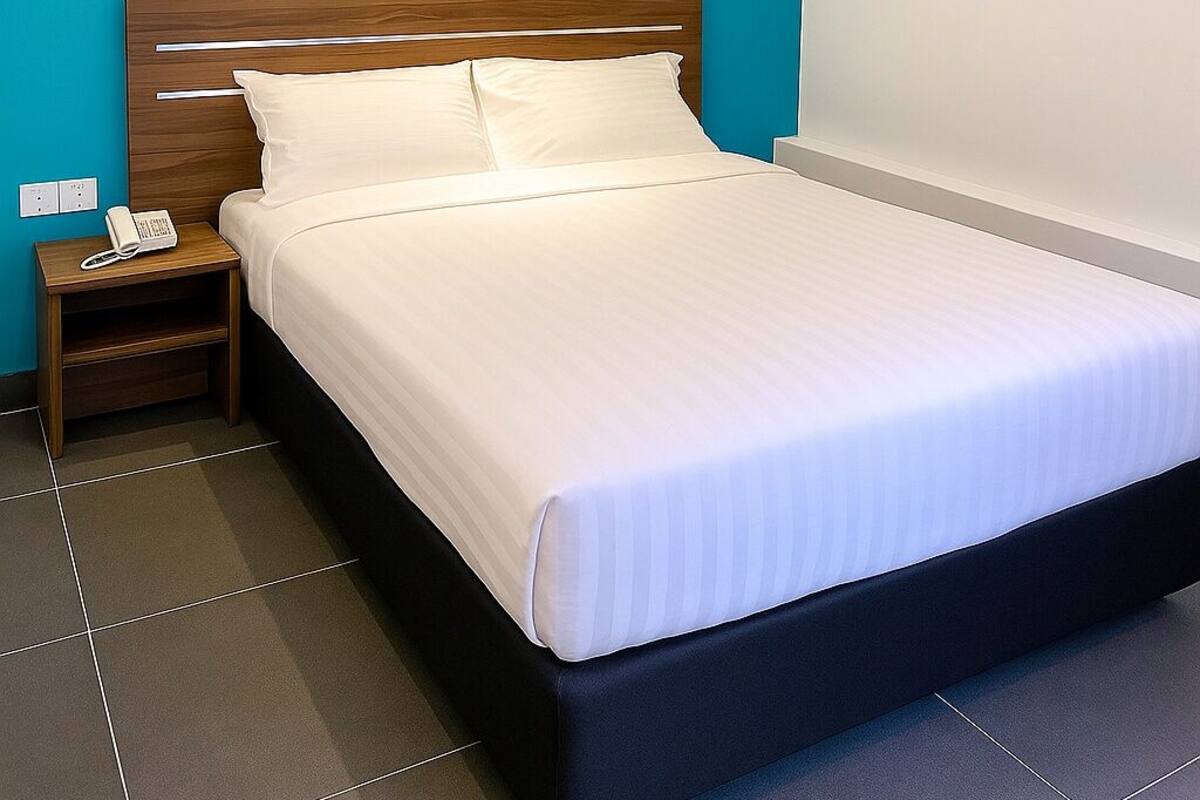 A neatly made bed in a room with a teal accent wall and a wooden headboard.