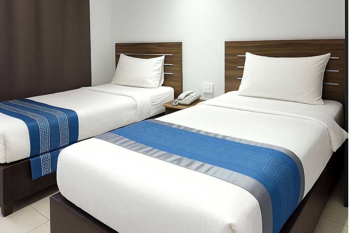 A hotel room with two beds, a nightstand with a phone, and a large window with curtains.