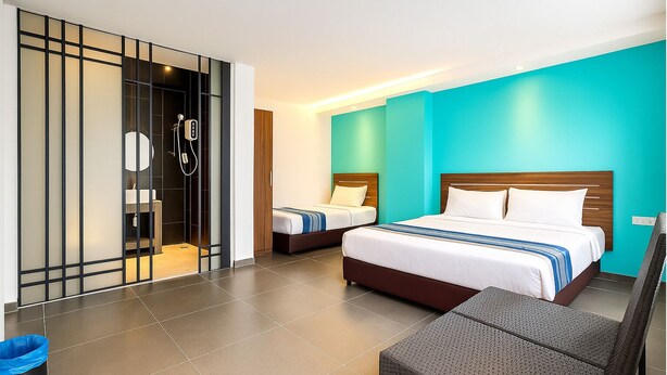 A hotel room with a large bed, two smaller beds, a bathroom with a shower, and a seating area with a chair and table. - Hotel 1915 Kuala Lumpur (Kuala Lumpur)