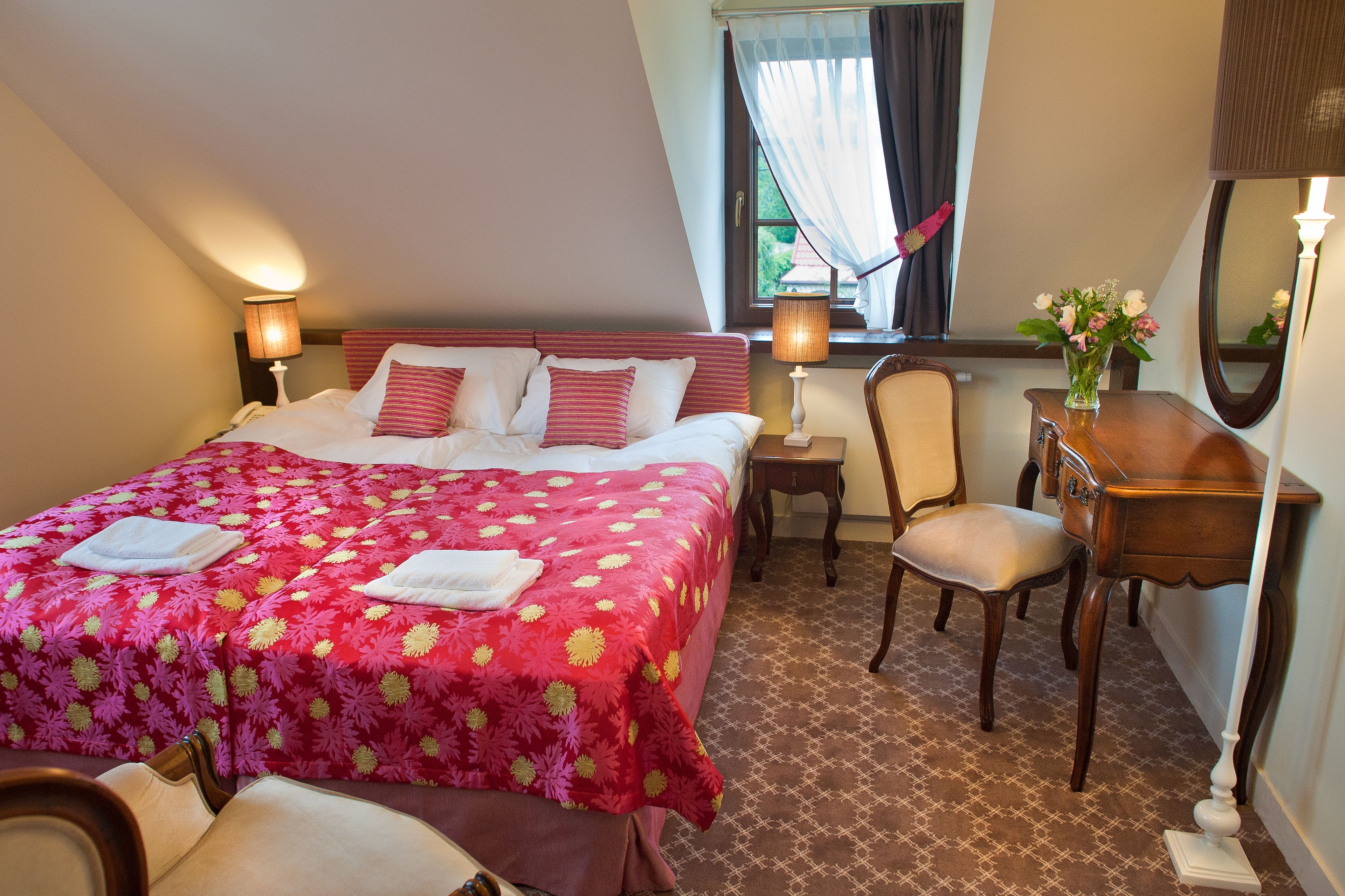 Une chambre d’hôtel avec un lit, un bureau, une chaise, un miroir et une fenêtre avec des rideaux.