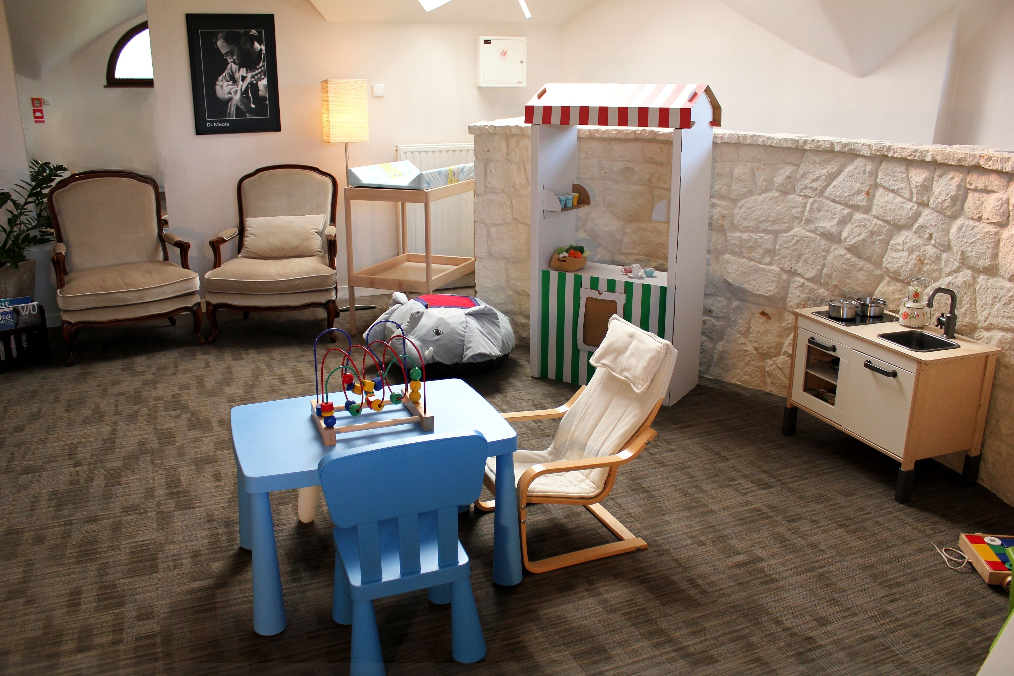 Una habitación acogedora con zona de juegos, que incluye una kitchenette pequeña, un sillón mecedora y una mesa con juguetes.