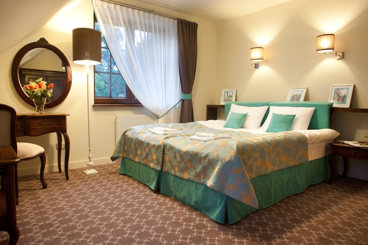 Ein ordentlich eingerichtetes Schlafzimmer mit einem Bett, einem Nachttisch, einem Stuhl, einem Spiegel und einem Fenster mit Vorhängen.