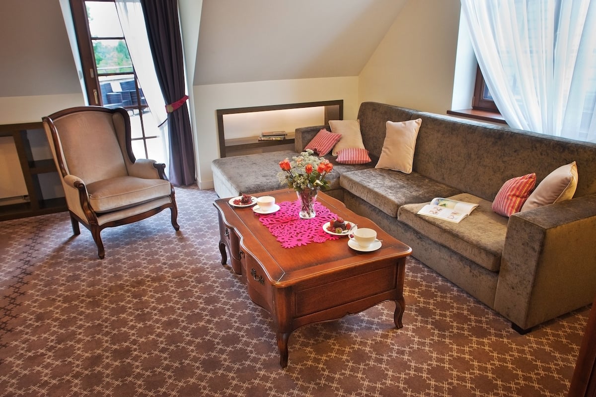 Ein gemütliches Zimmer mit Holzstuhl, einer Couch und einem Couchtisch mit Blumen in einer Vase.