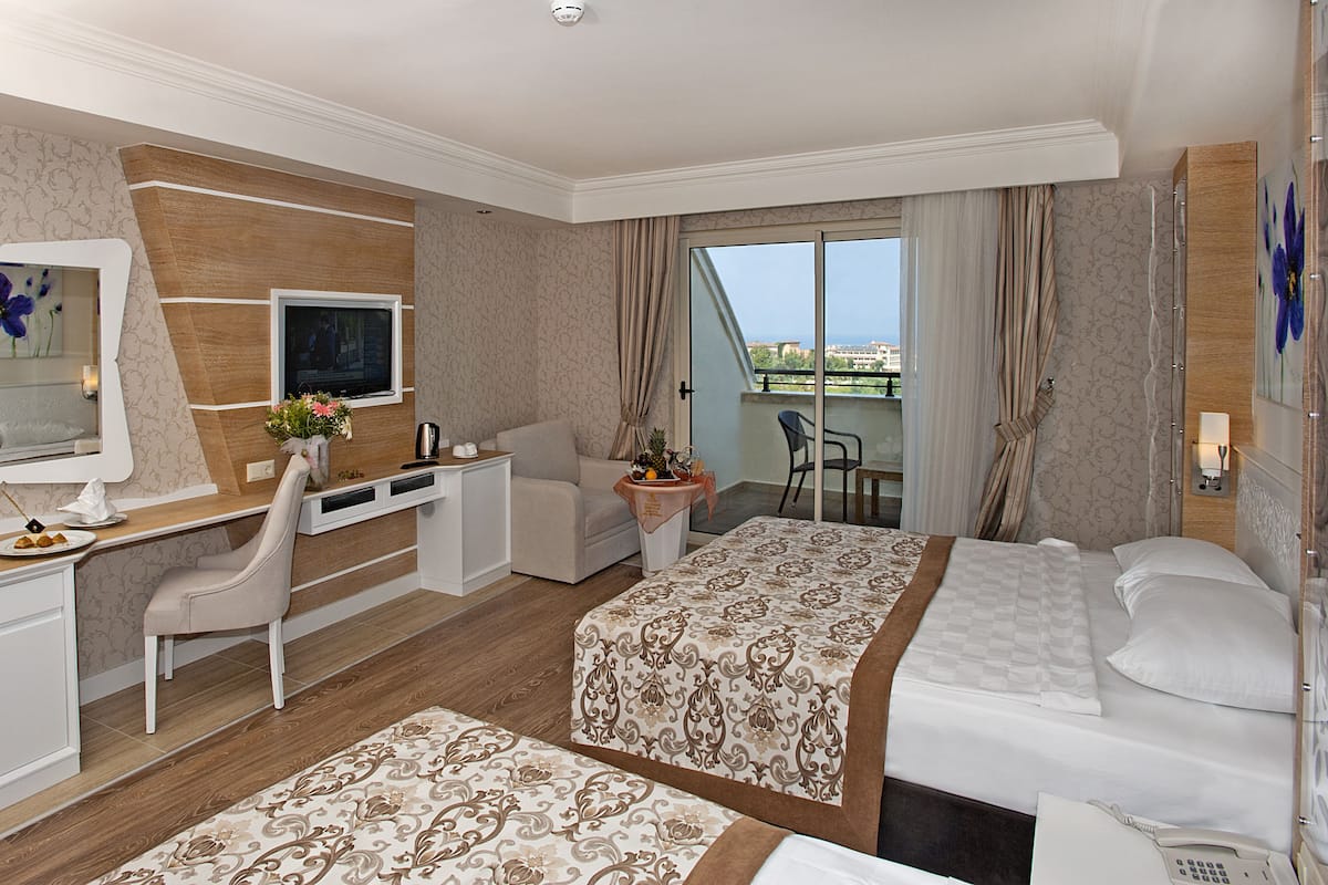 A hotel room with a bed, desk, chair, and a view of the city through the window.