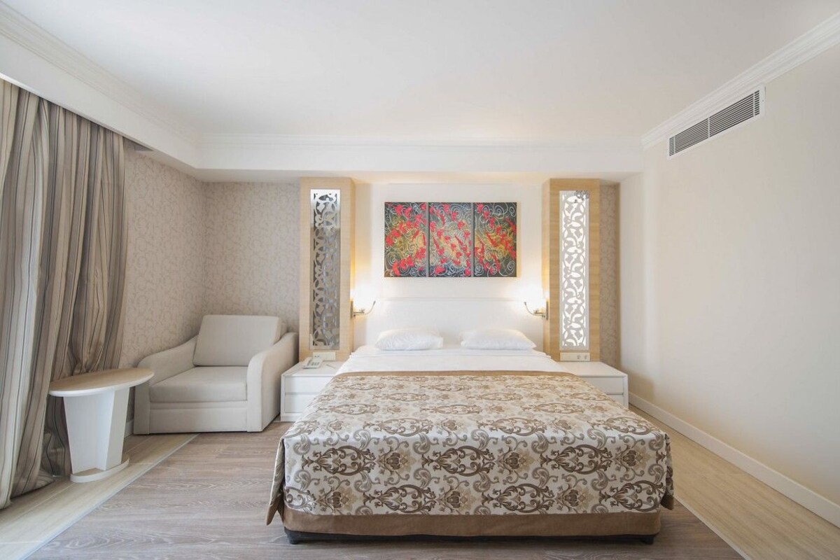 A hotel room with a large bed, a sofa, a small table, and a decorative wall piece.