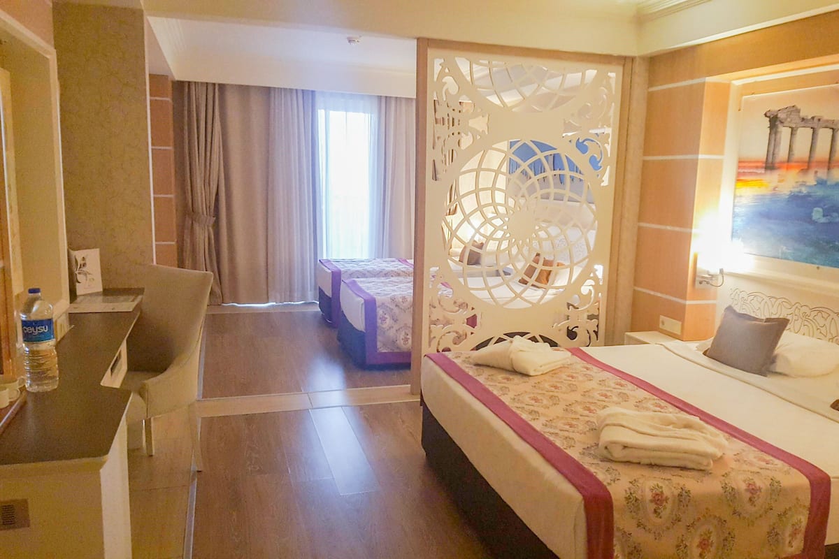 A hotel room with a bed, a desk, a chair, a water bottle, and a painting on the wall.