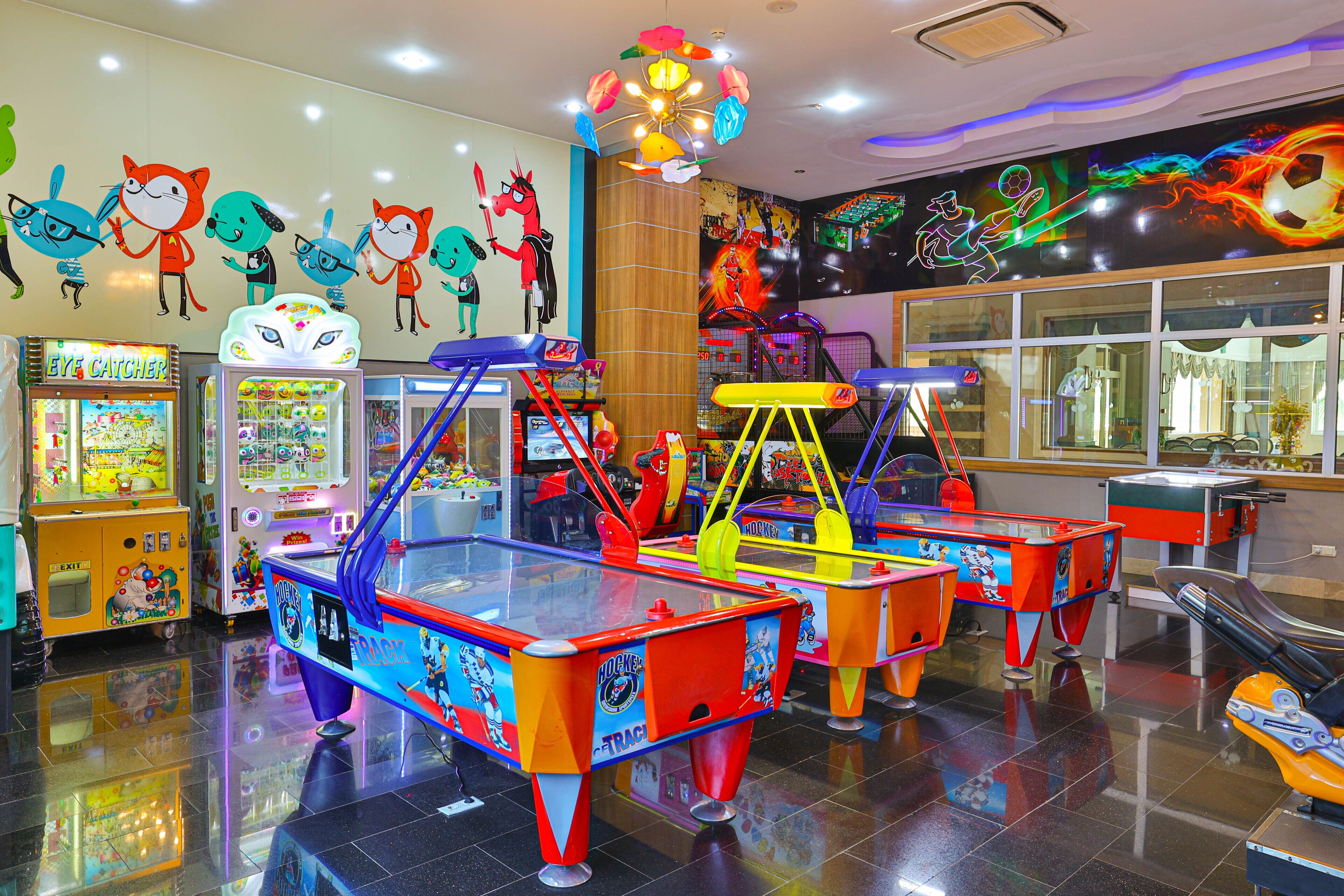 Un salón de juegos muy iluminado con diversas máquinas, incluyendo una mesa de ping pong y máquinas de pinzas.
