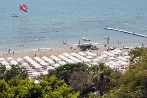 A beach with numerous white umbrellas, a pier extending into the water, and several boats.