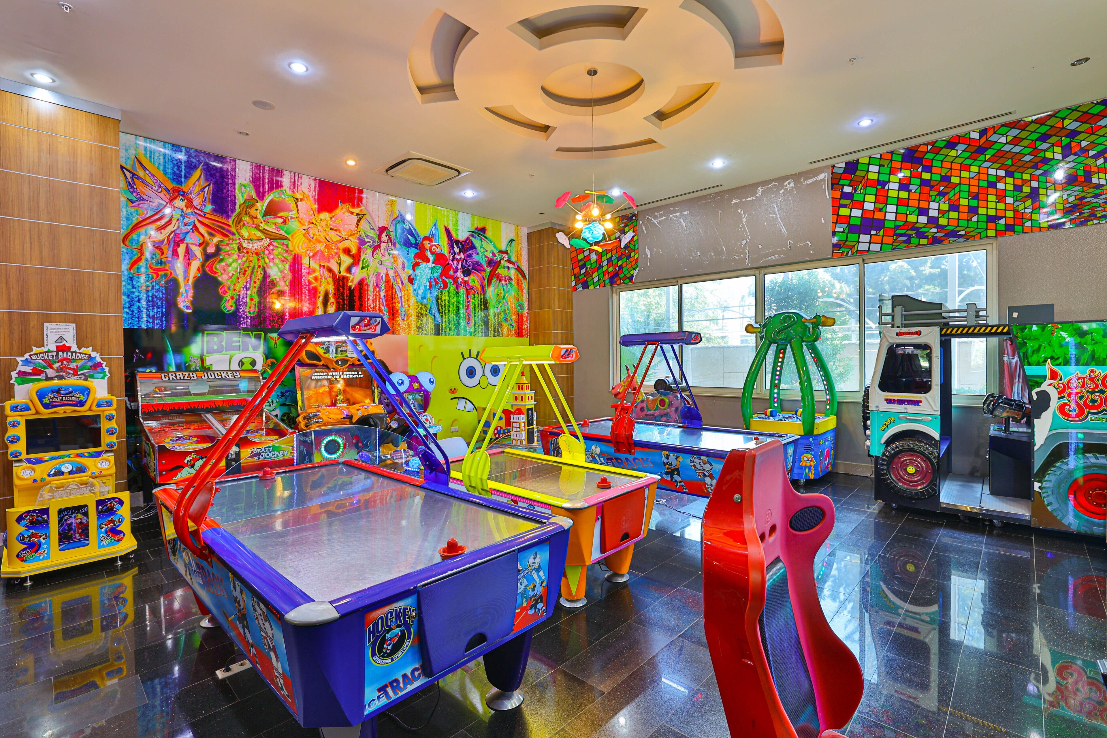 A brightly lit indoor play area with various colorful arcade games and rides, including a train ride and a red slide.
