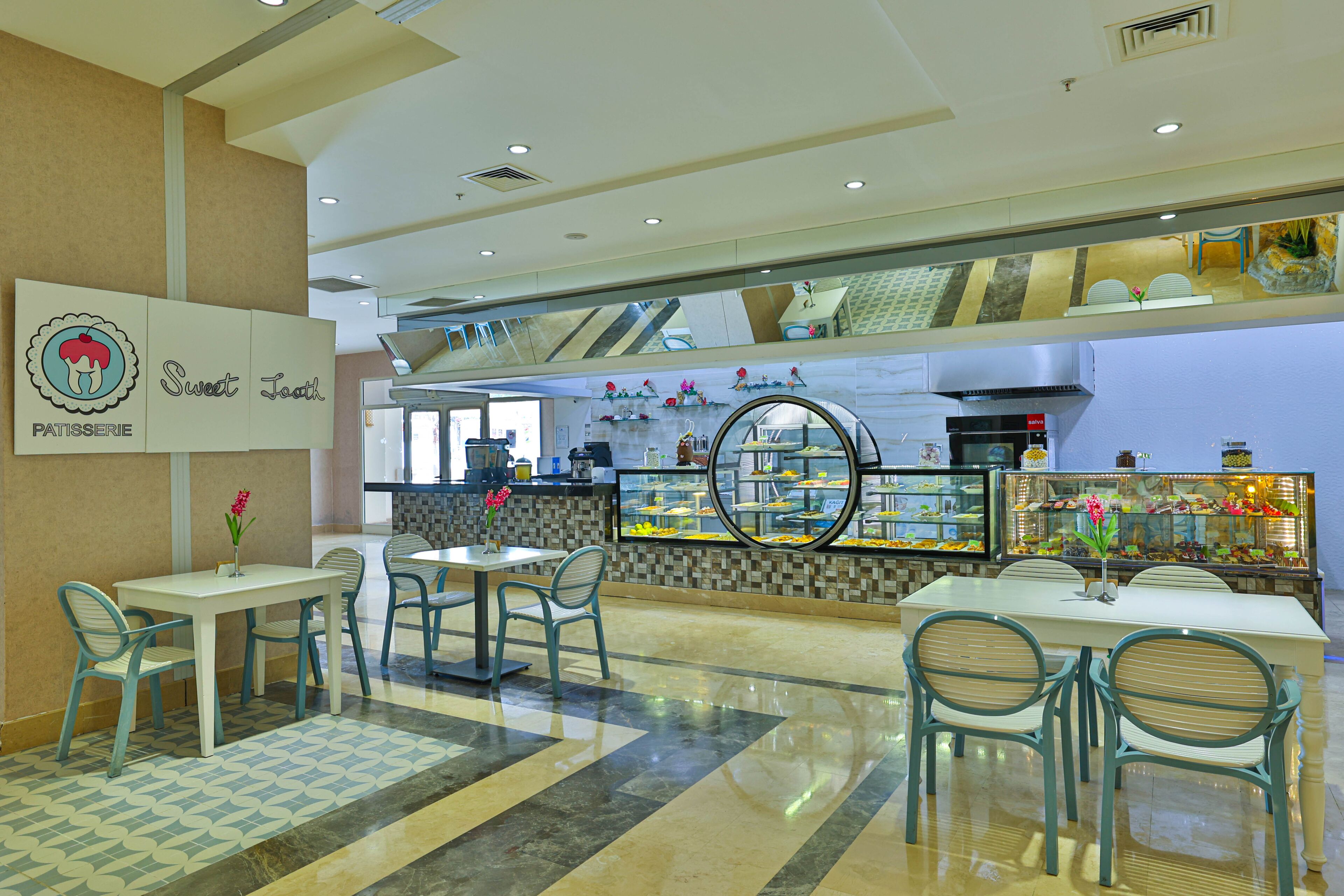 A patisserie with a modern interior, featuring a central display case, seating area with tables and chairs, and a decorative wall with a mosaic pattern.