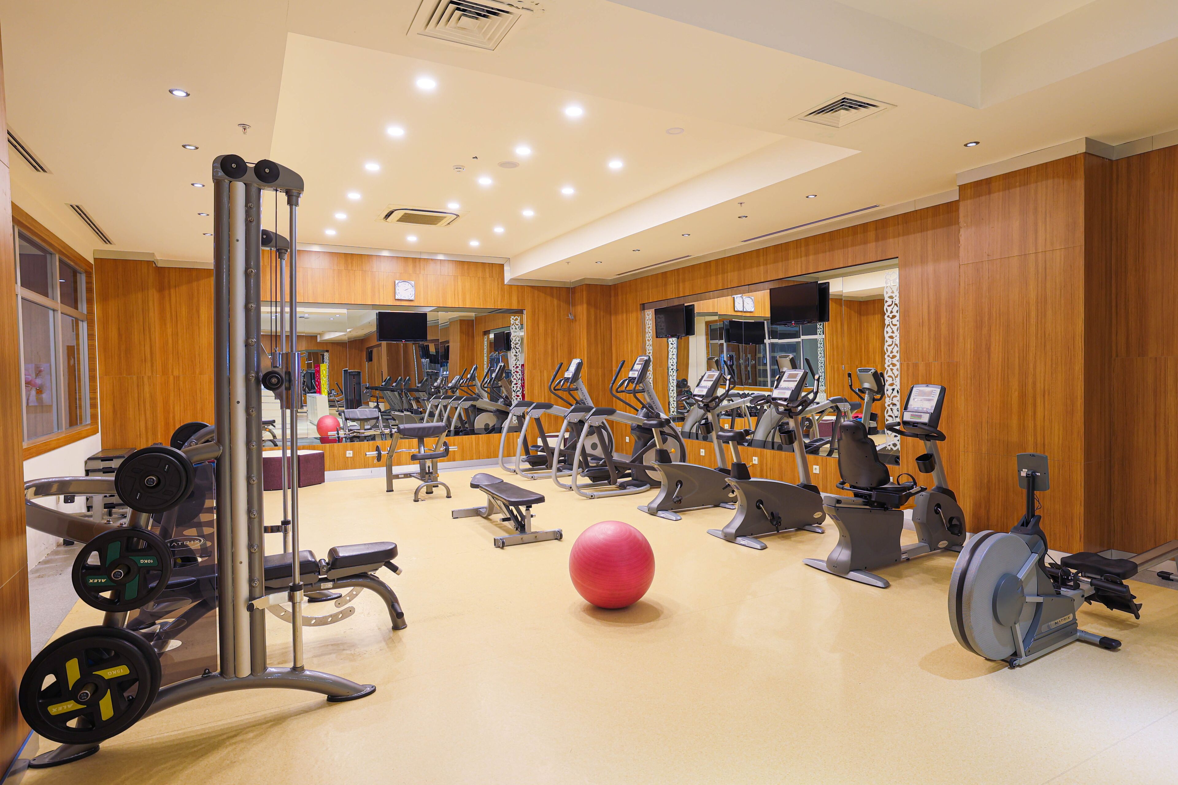 Een fitnessruimte met diverse trainingsapparaten, waaronder loopbanden, hometrainers en krachtapparaten.