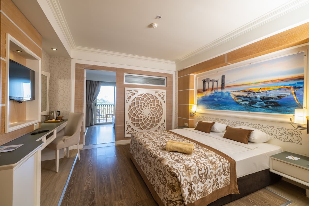 A hotel room with a bed, a desk, a chair, a TV, and a painting on the wall.