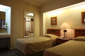 Habitación de hotel con dos camas, un escritorio, un espejo, una lámpara y un cuadro en la pared.