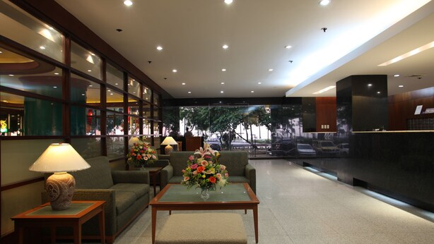 A lobby with a reception desk, seating area, and a view of the street through large windows. - Sunny Bay Suites (Manila)