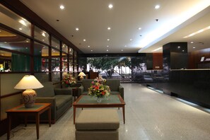 A lobby with a reception desk, seating area, and a view of the street through large windows. - Sunny Bay Suites (Manila)