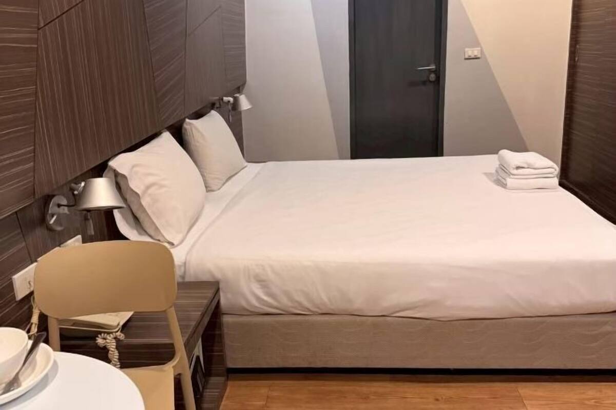 A neatly made bed with white linens, a bedside table with a lamp, and a chair.