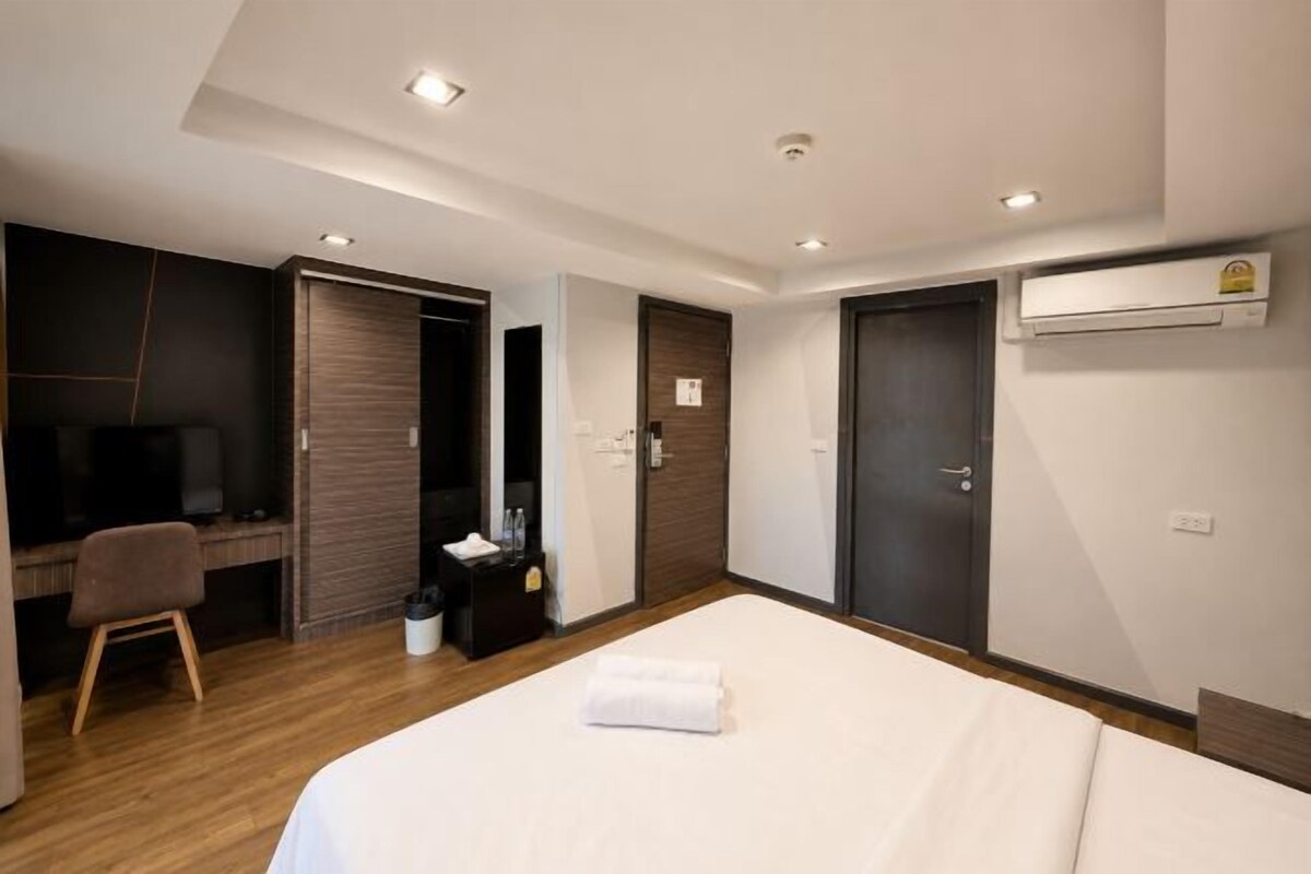 A hotel room with a bed, a desk with a chair, a TV, and a wardrobe.