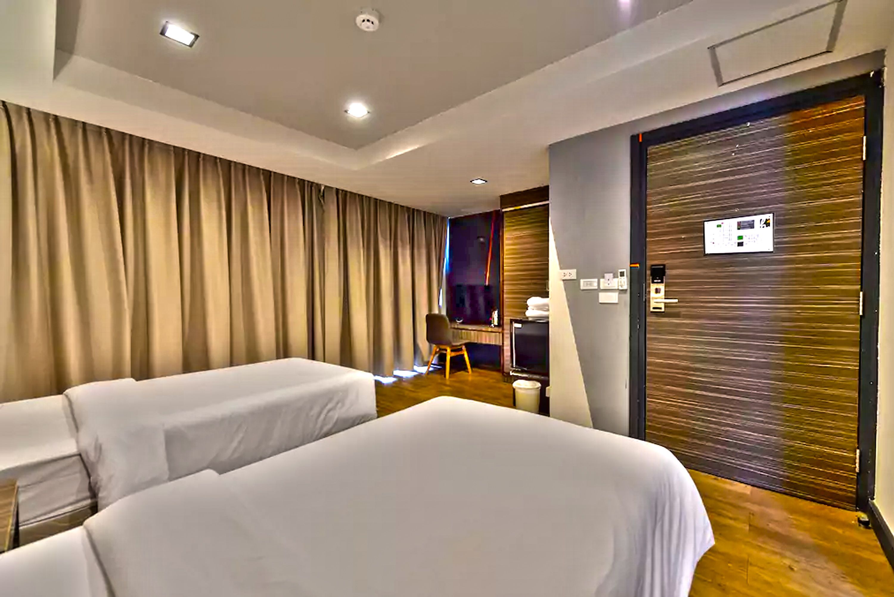 Habitación de hotel con dos camas, un escritorio, una silla, un televisor y una puerta con panel de control.