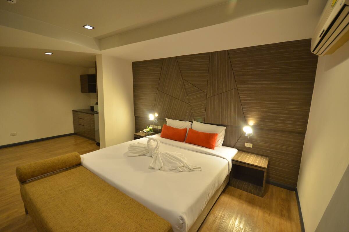 A modern hotel room with a large bed, wooden headboard, bedside tables with lamps, and a flat-screen TV mounted on the wall.