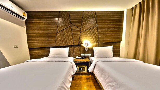 A hotel room with two beds, wooden headboard, bedside tables, and an air conditioning unit. - H2 Hotel (Bangkok)