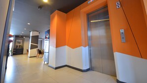 A hallway with orange and white walls, a door, and an elevator. - H2 Hotel (Bangkok)