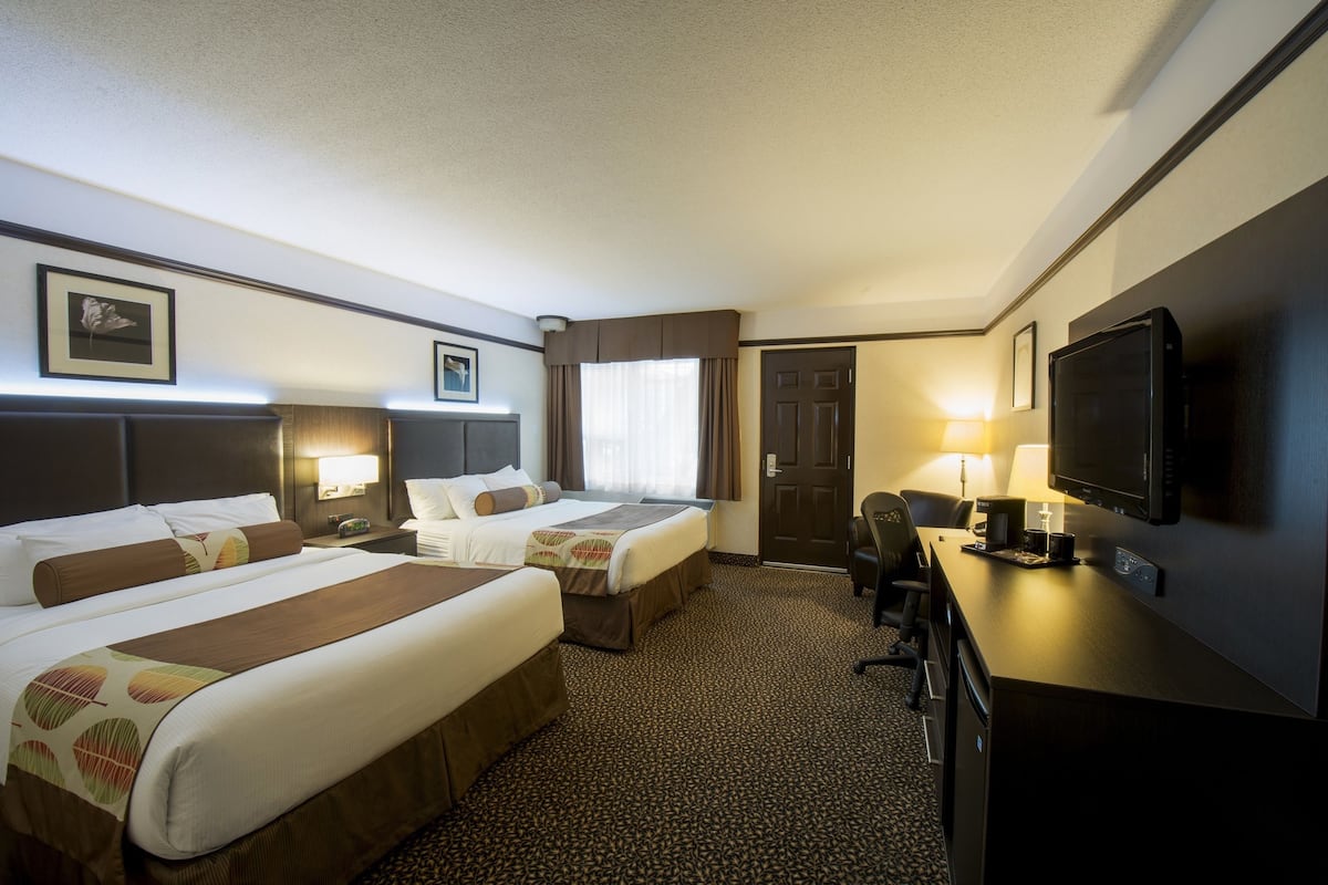 A hotel room with two beds, a desk, a television, and a door.