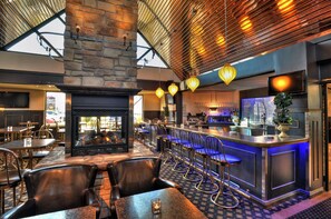 Un restaurante con chimenea de piedra, zona de bar con taburetes y un techo alto con vigas a la vista.