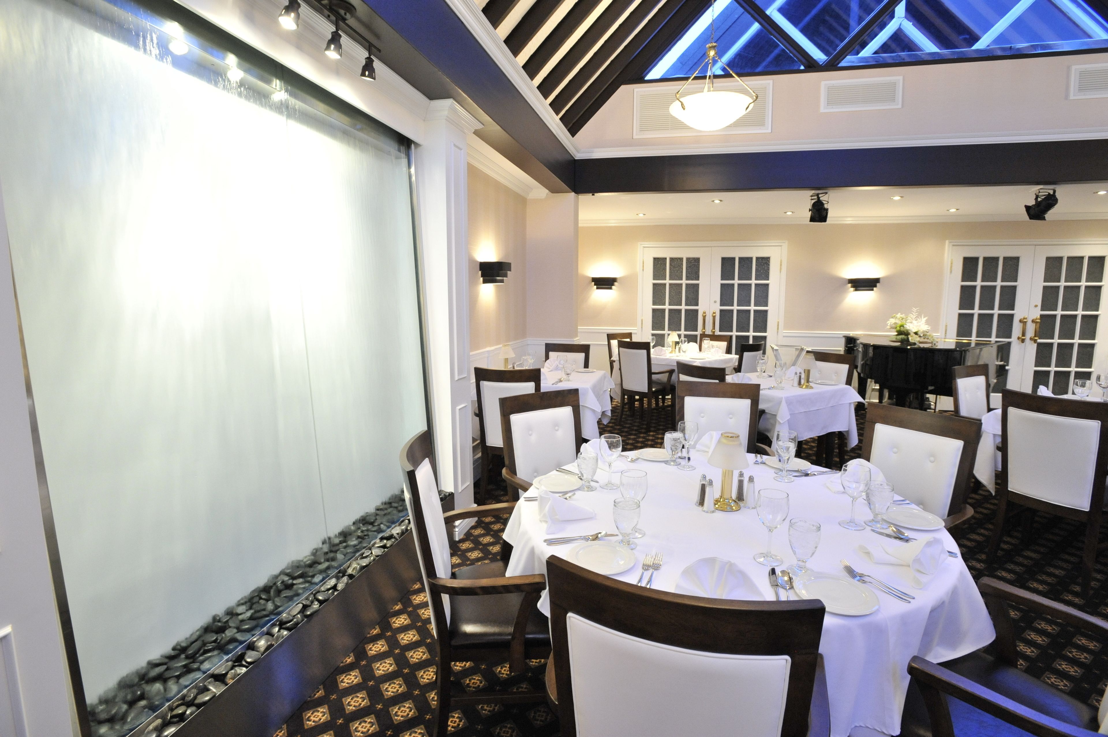 Un espace repas avec plusieurs tables rondes dressées pour un repas, chacune étant recouverte d’une nappe blanche et agrémentée de chaises et de couverts.