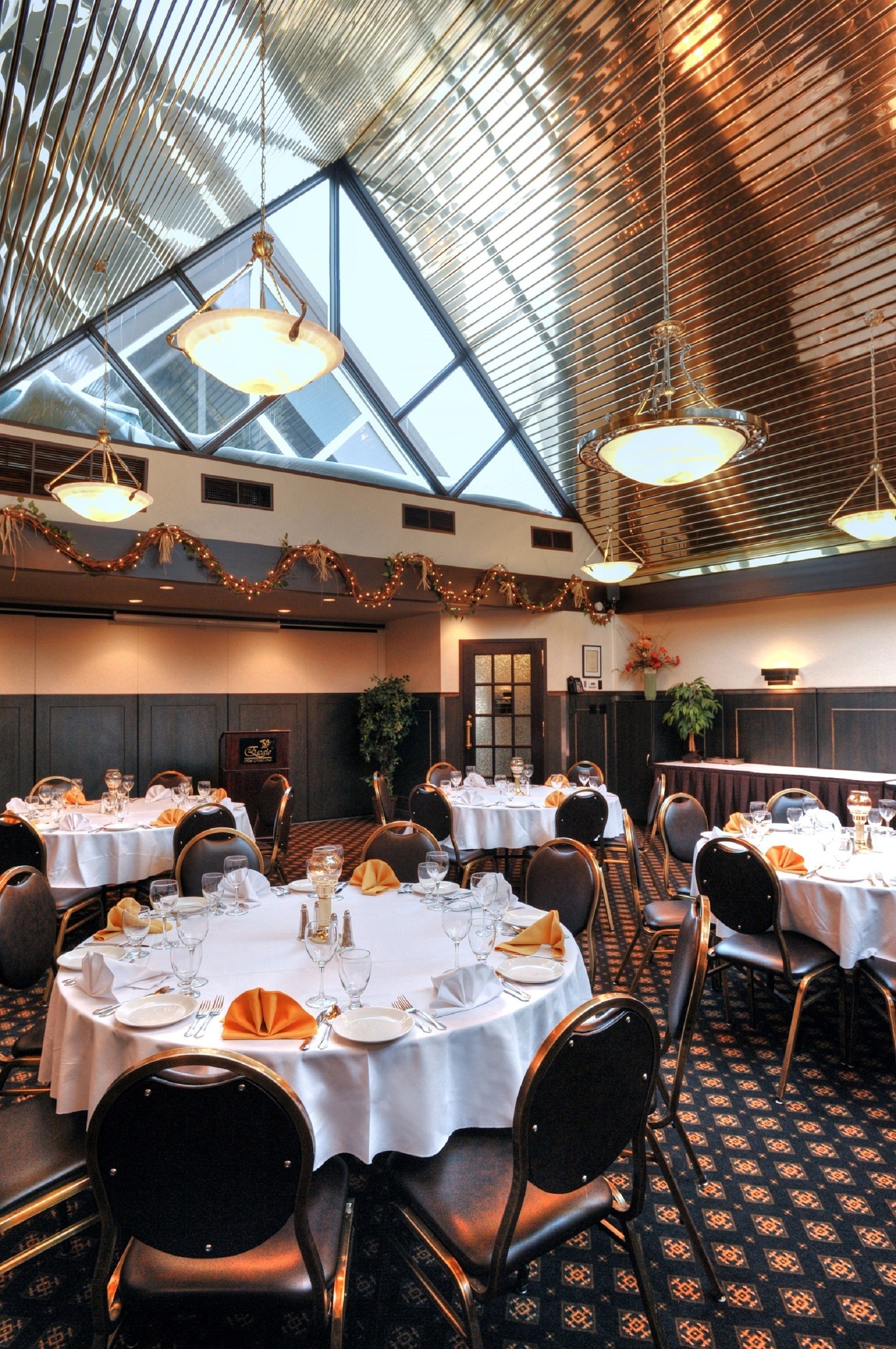 A banquet hall with round tables, black chairs, and a high ceiling with a skylight.