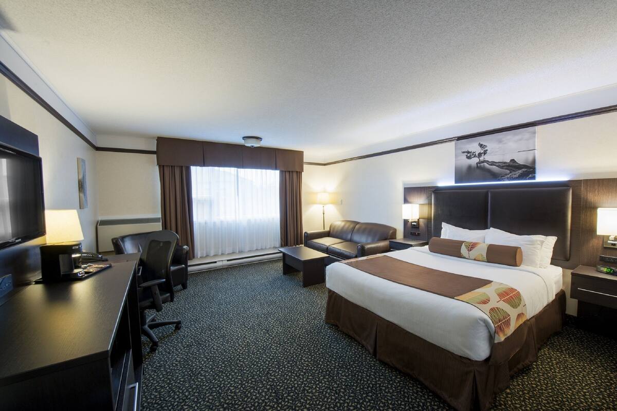 A hotel room with a large bed, a desk with a computer, a chair, a sofa, and a TV.