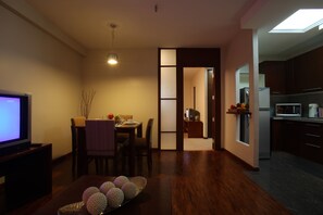 Una sala de estar moderna con televisor, mesa de comedor y esferas decorativas. Se ve una cocina con electrodomésticos al fondo.