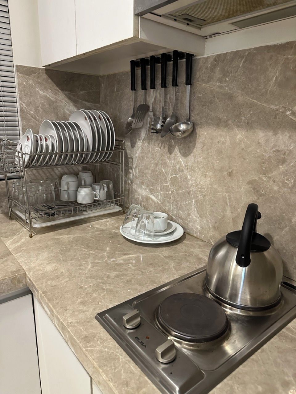 Une cuisine équipée d’une cuisinière en acier inoxydable, d’une bouilloire et d’un égouttoir à vaisselle contenant des assiettes et des tasses.