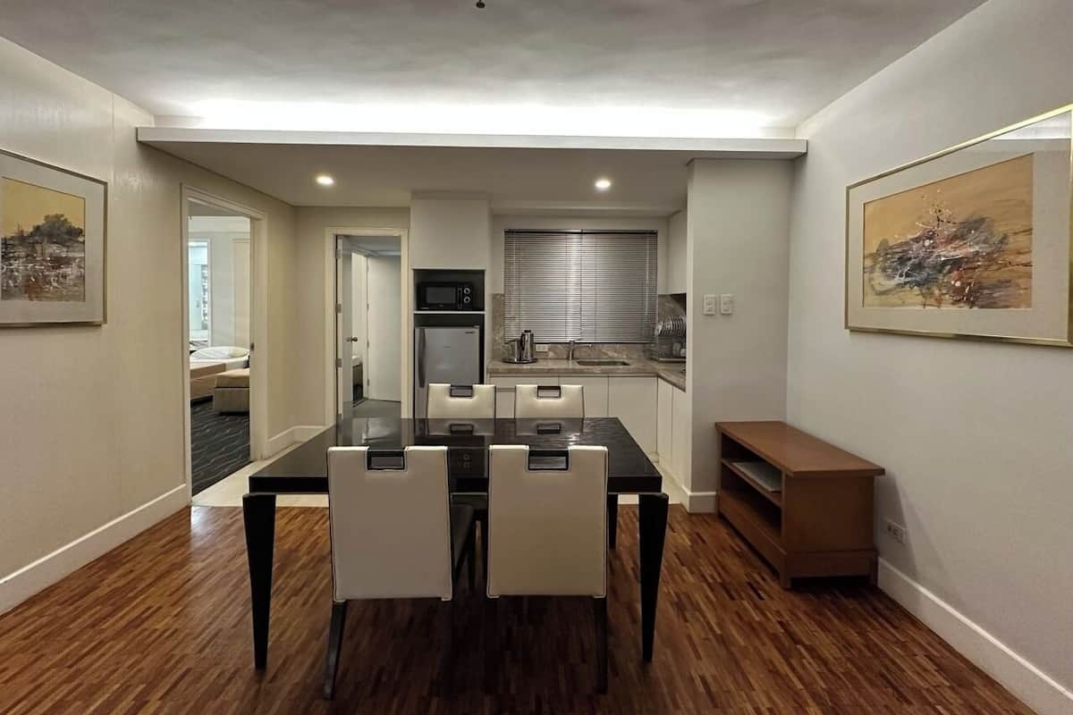 A modern kitchen with a dining area, featuring a black table and white chairs, a built-in oven, and a window with blinds.