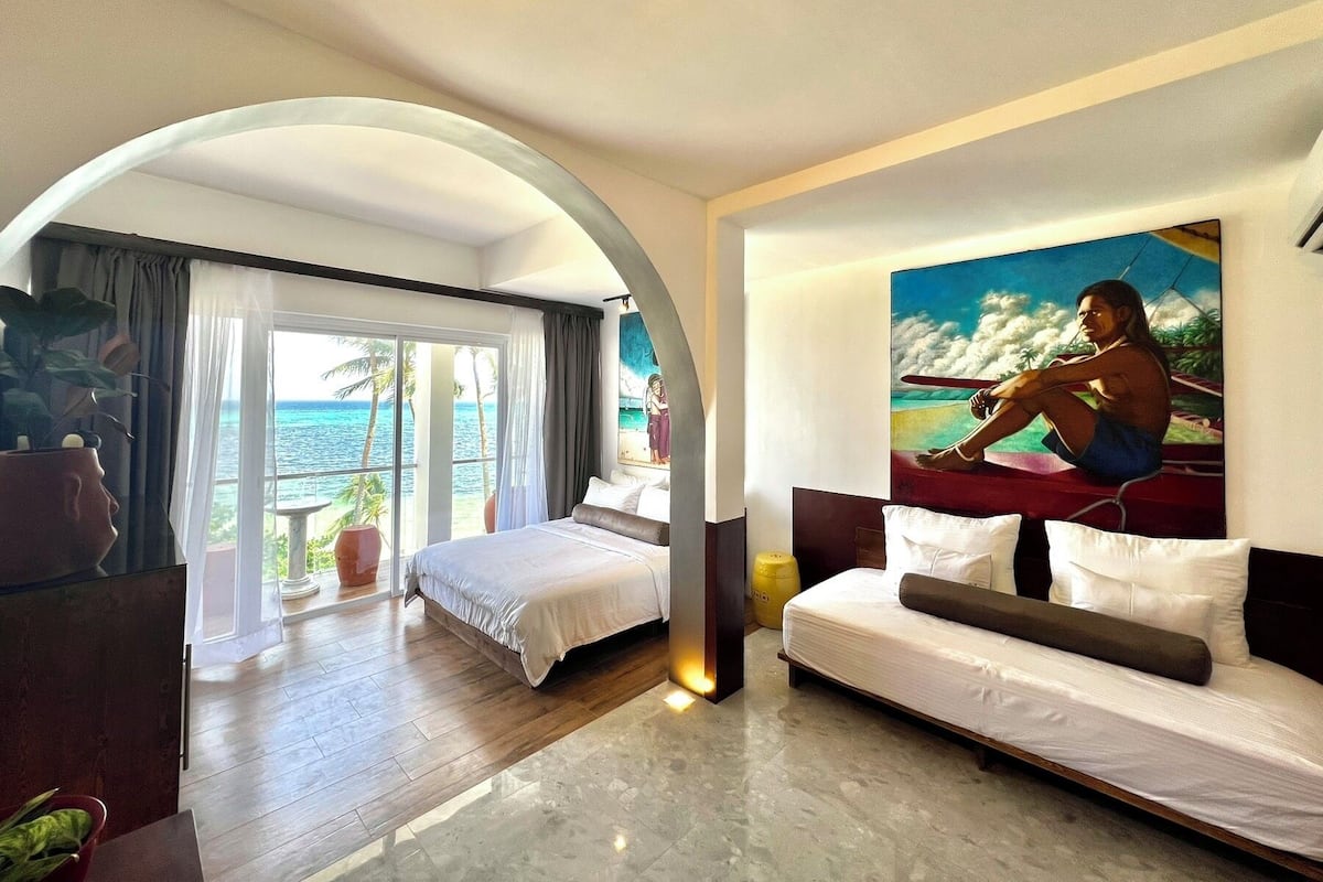 Une chambre d’hôtel avec un lit, un tableau, une plante et une vue sur l’océan.