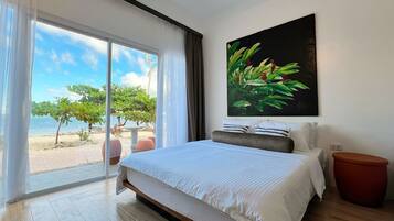 Un dormitorio con una cama grande, vista a la playa y un cuadro de follaje en la pared.