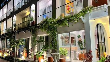 Um hotel de vários andares com varandas, plantas em vasos e uma entrada bem iluminada.