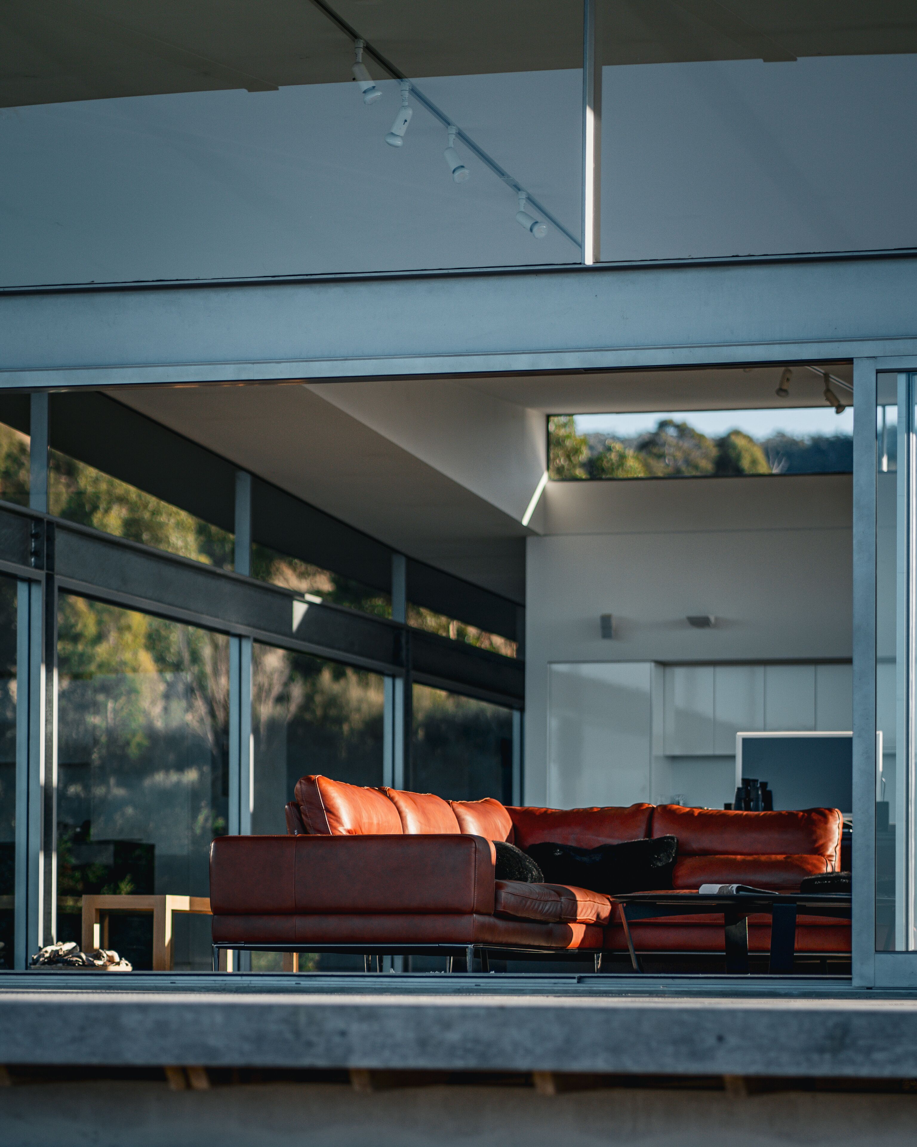 Uma sala de estar moderna com um sofá de couro, uma mesa de centro e vista para o exterior através de grandes janelas.
