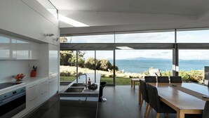 Une cuisine moderne dotée d’un grand îlot central, d’un coin repas avec une table en bois et d’une vue sur la mer.