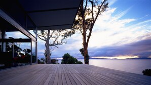 Une terrasse extérieure moderne offrant une vue sur la mer et un arbre.