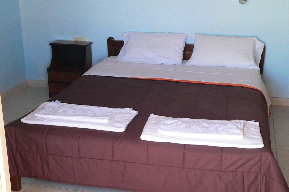 A neatly made bed with a brown bedspread, two white pillows, and two folded towels on the bed.