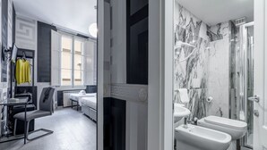 Een moderne hotelkamer met een bed, een bureau en een stoel. Er is een badkamer met een douche, toilet en een douchetoilet. De kamer heeft een groot raam en een deur die naar een andere kamer leidt.