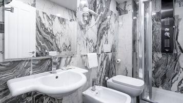 A modern bathroom with a marble backsplash, a sink, bidets, a toilet, and a glass-enclosed shower area.
