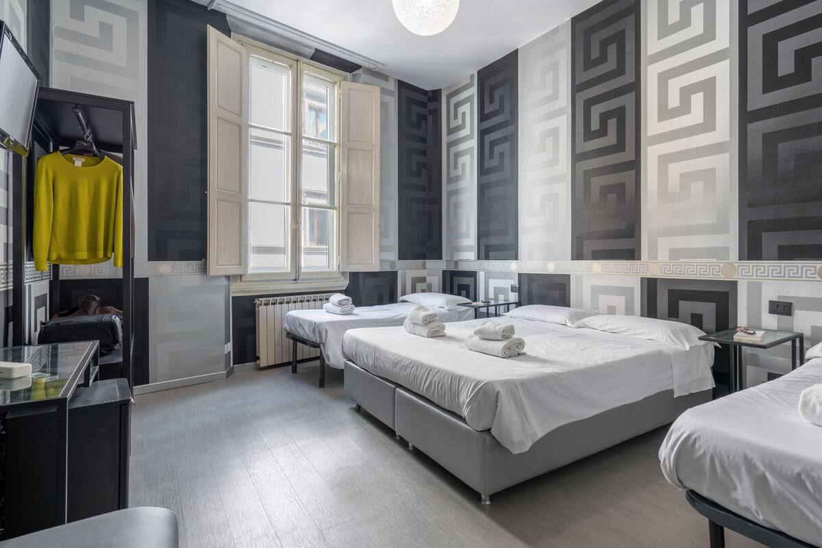 Habitación de hotel con dos camas, un escritorio, una silla, un radiador y una ventana.