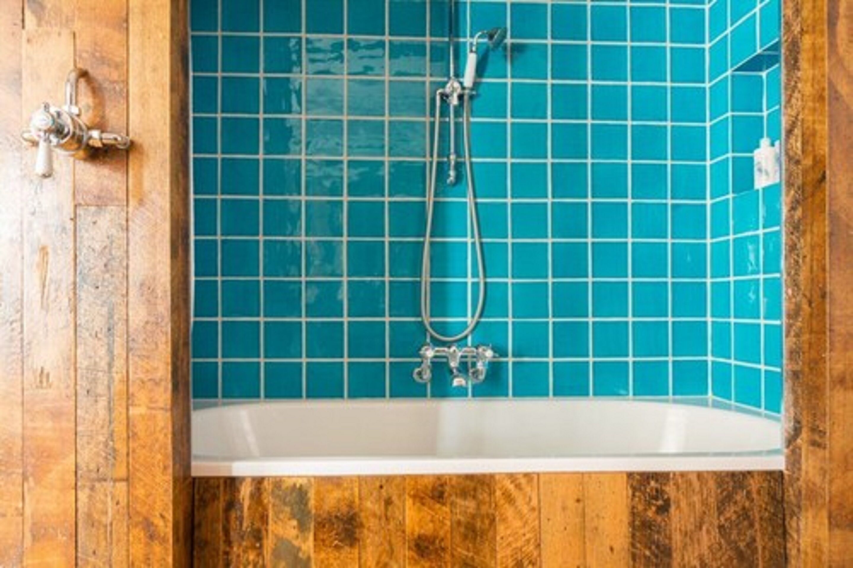 A bathroom with a wooden door and a bathtub with blue tiles.