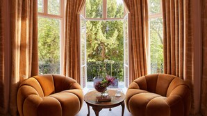 Une pièce avec deux fauteuils, une petite table et une vue sur un balcon bordé d’arbres.